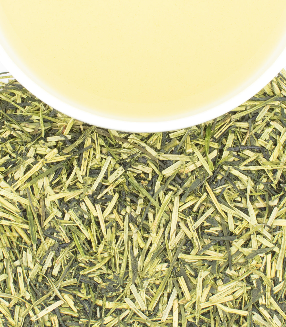 A cup of kukicha tea surrounded by dried green tea twigs and leaves, showcasing its vibrant yellow-green color.