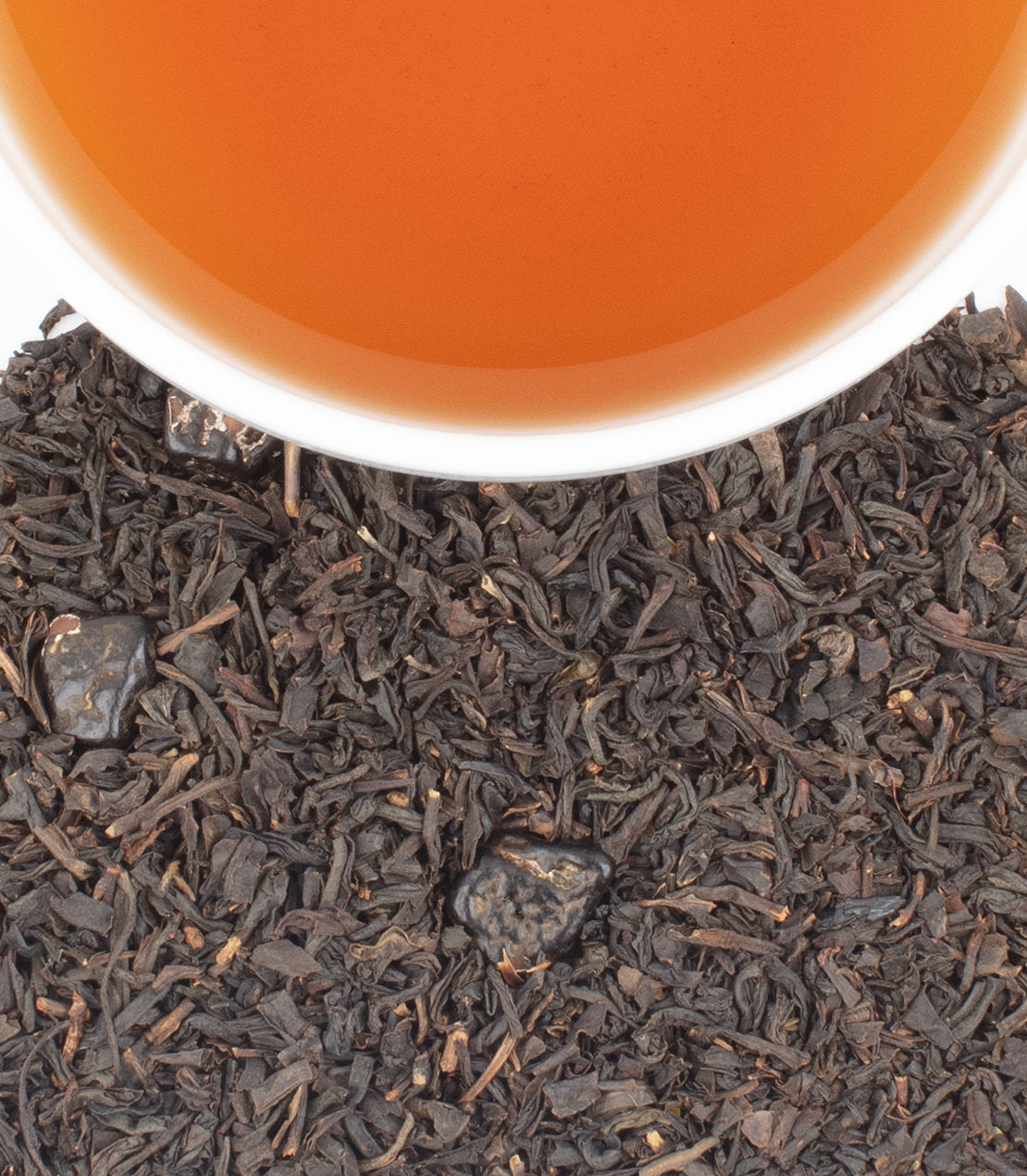 Close-up of loose-leaf tea leaves in dark brown and black tones, with a white cup rim and amber tea visible at the top.