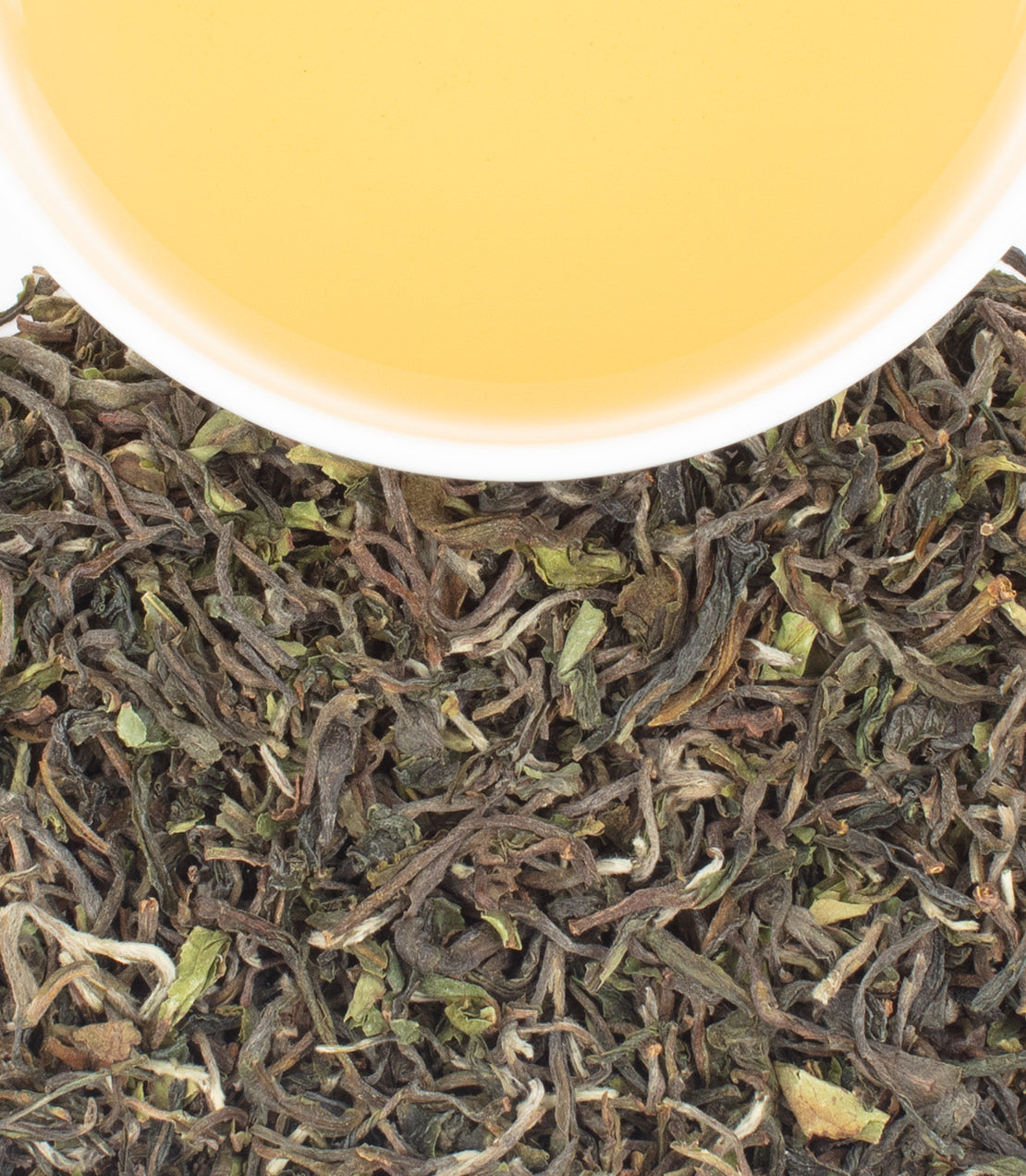 A cup of golden tea sits above a pile of dried, twisted tea leaves.