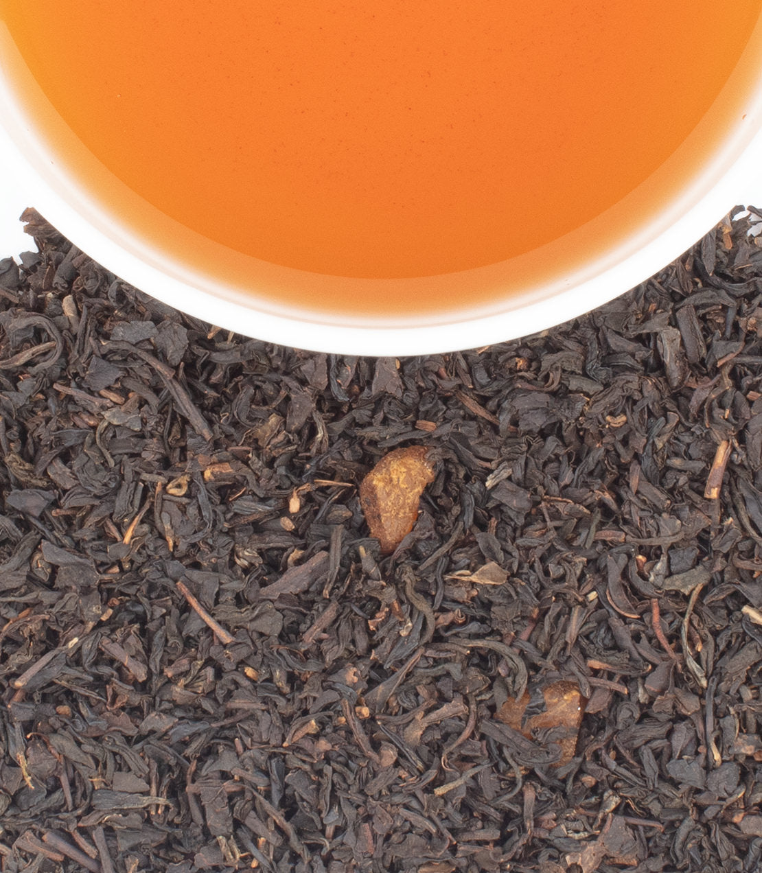 Dark tea leaves with apricot pieces sit below an amber cup of brewed tea in a white cup.