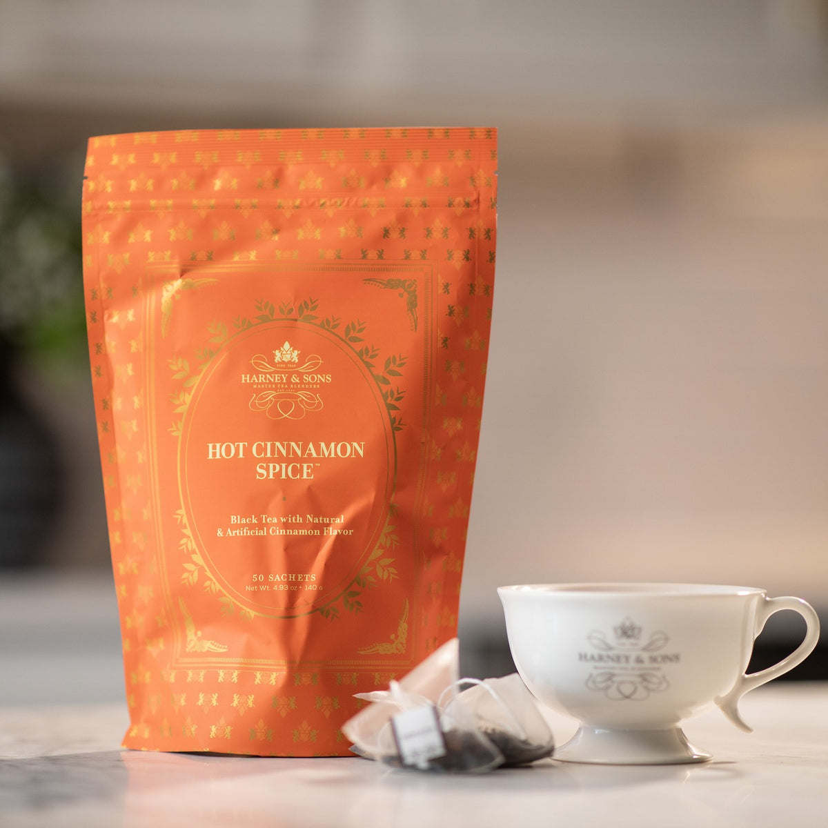 Hot Cinnamon Spice Bag of 50 Sachets on a marble kitchen counter beside a tea sachet and a white teacup