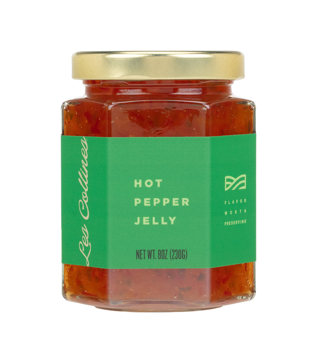 A hexagonal glass jar with a gold lid contains red hot pepper jelly, labeled with a green sticker indicating the brand "Les Collines" and the product name "Hot Pepper Jelly."