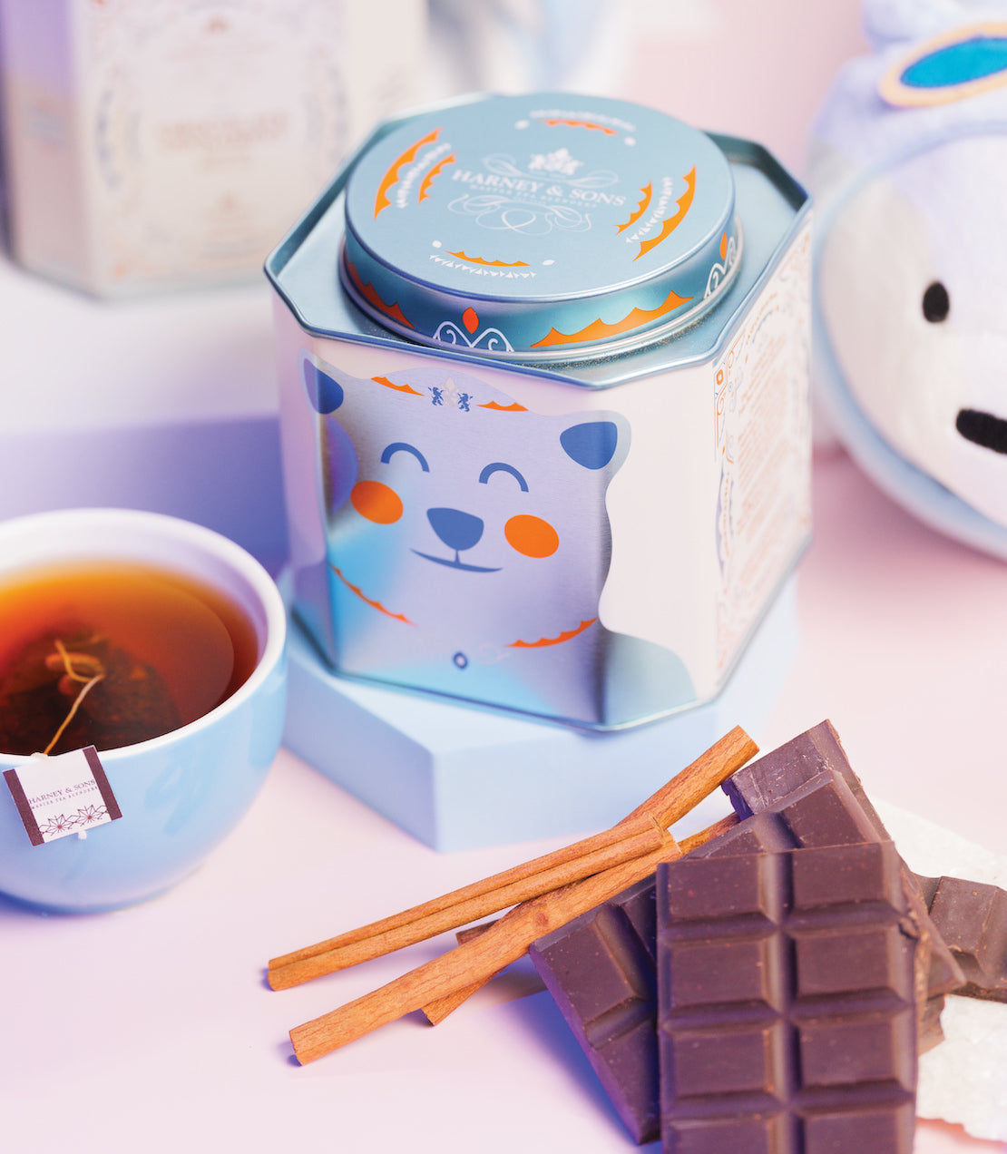 Tin of 30 Chocolate Cinnamint sachets with a bear design, cinnamon sticks, chocolate, and a cup of tea.