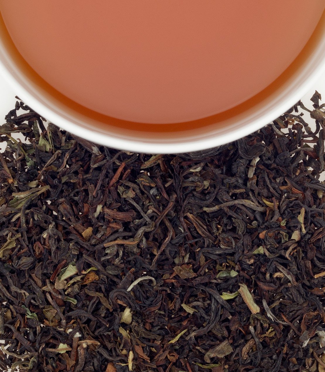 Darjeeling tea in a cup above loose tea leaves, showcasing a rich amber color and aromatic blend.