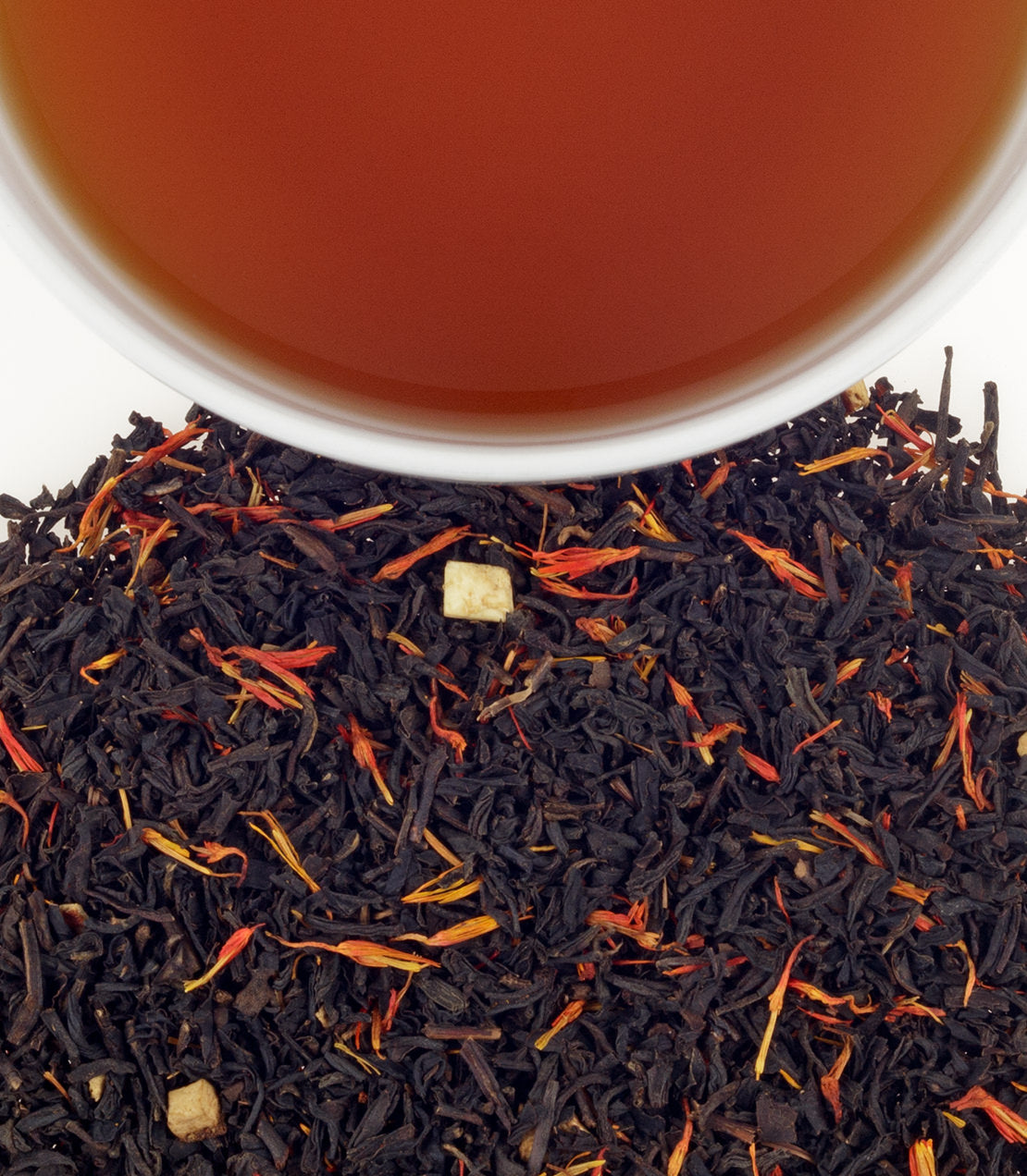 Close-up of loose-leaf tea with dark black tea leaves mixed with orange and yellow flower petals, with a white cup rim and amber tea visible at the top.