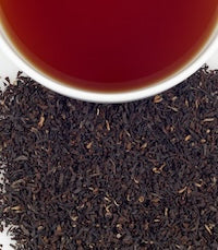 A white tasting cup with black tea brewed, and dark leaves around it. 