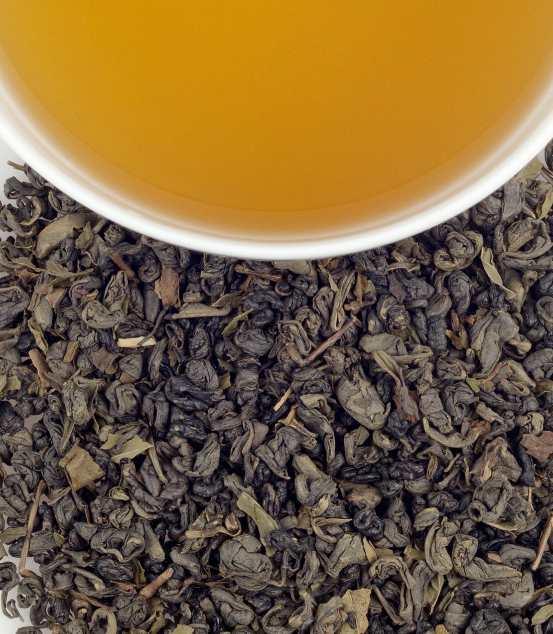 A white cup filled with golden tea sits above a pile of dark, twisted loose-leaf tea.