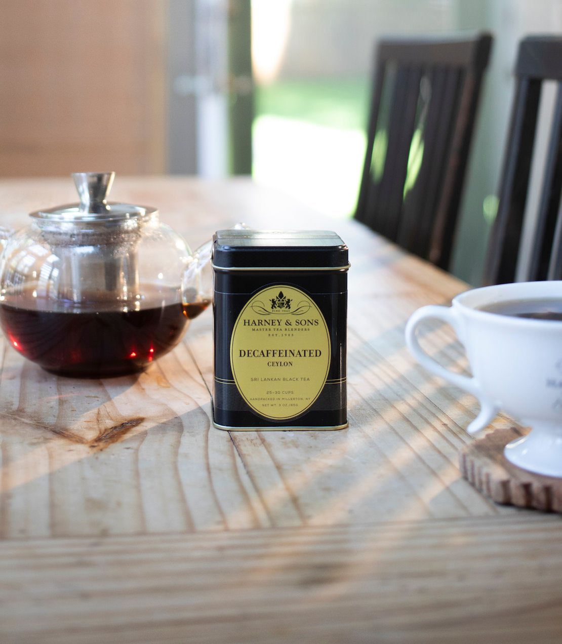Decaffeinated tea tin on a wooden table with a teacup and teapot in the background.
