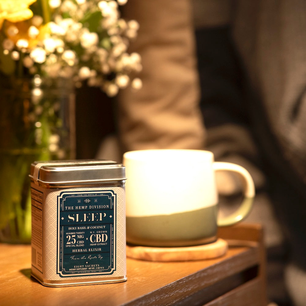 The Hemp Division's Sleep Tin of 8 Sachets on a bedside table next to a mug