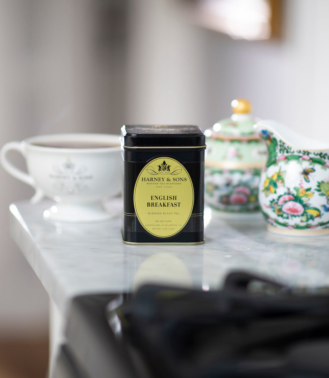 English Breakfast tea tin on a table with a floral teacup and sugar bowl in the background.