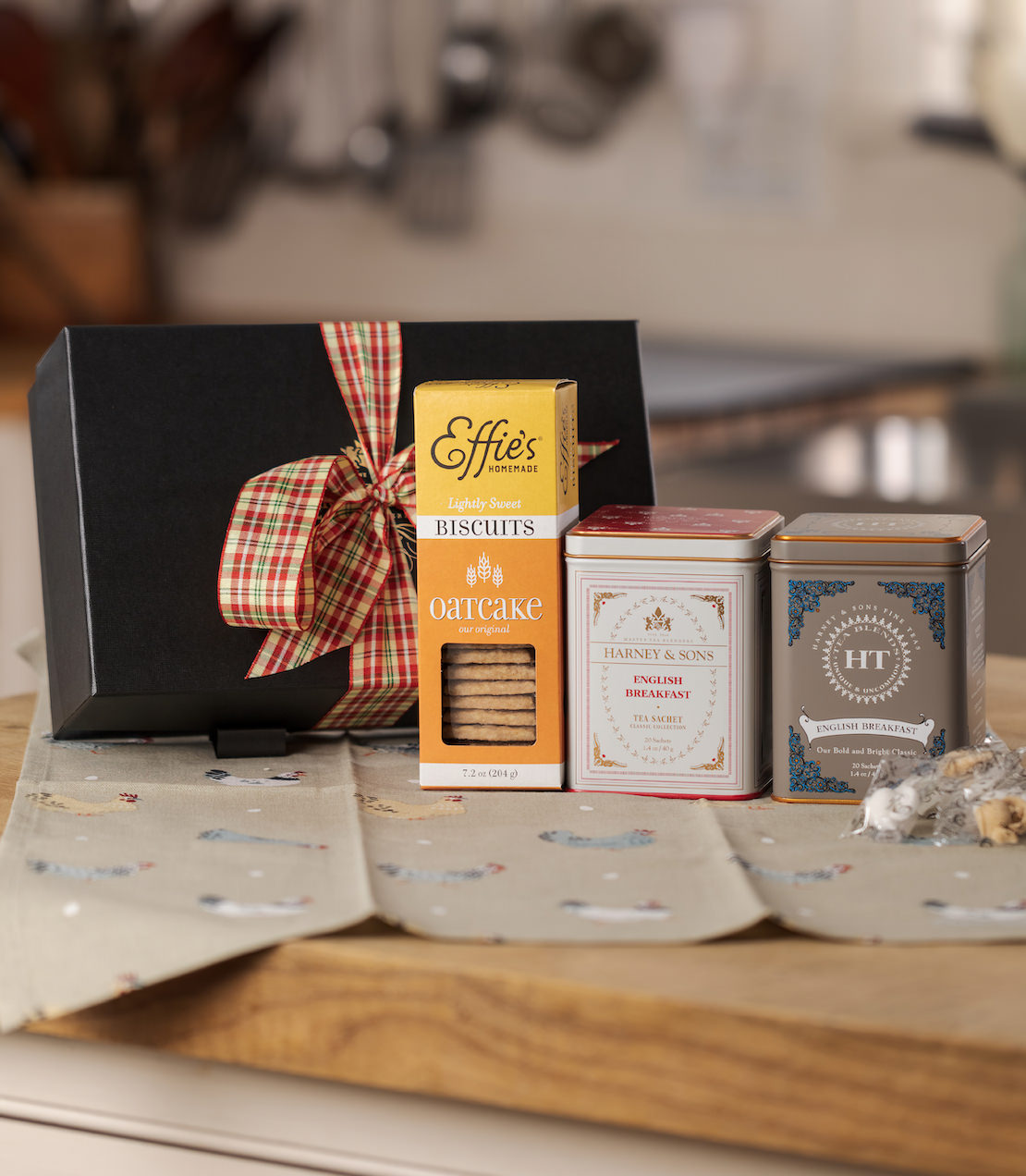 Two English Breakfast tea tins and a box of biscuits with a black gift box with a bow on a wooden surface.