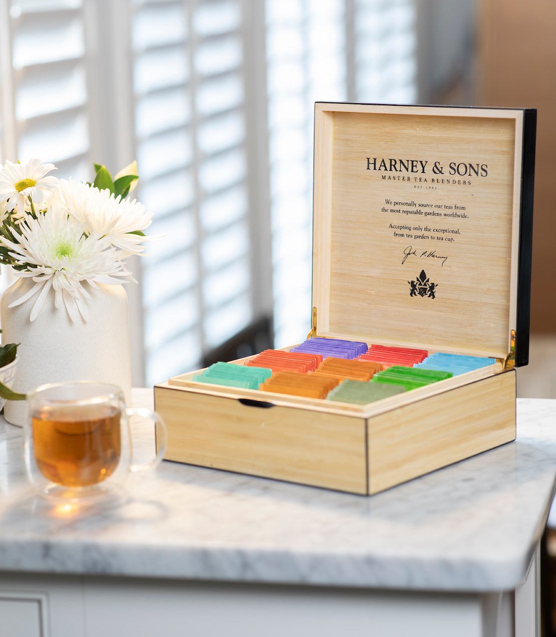 Harney & Sons tea box with colorful tea bags on a marble surface with a blurred background.