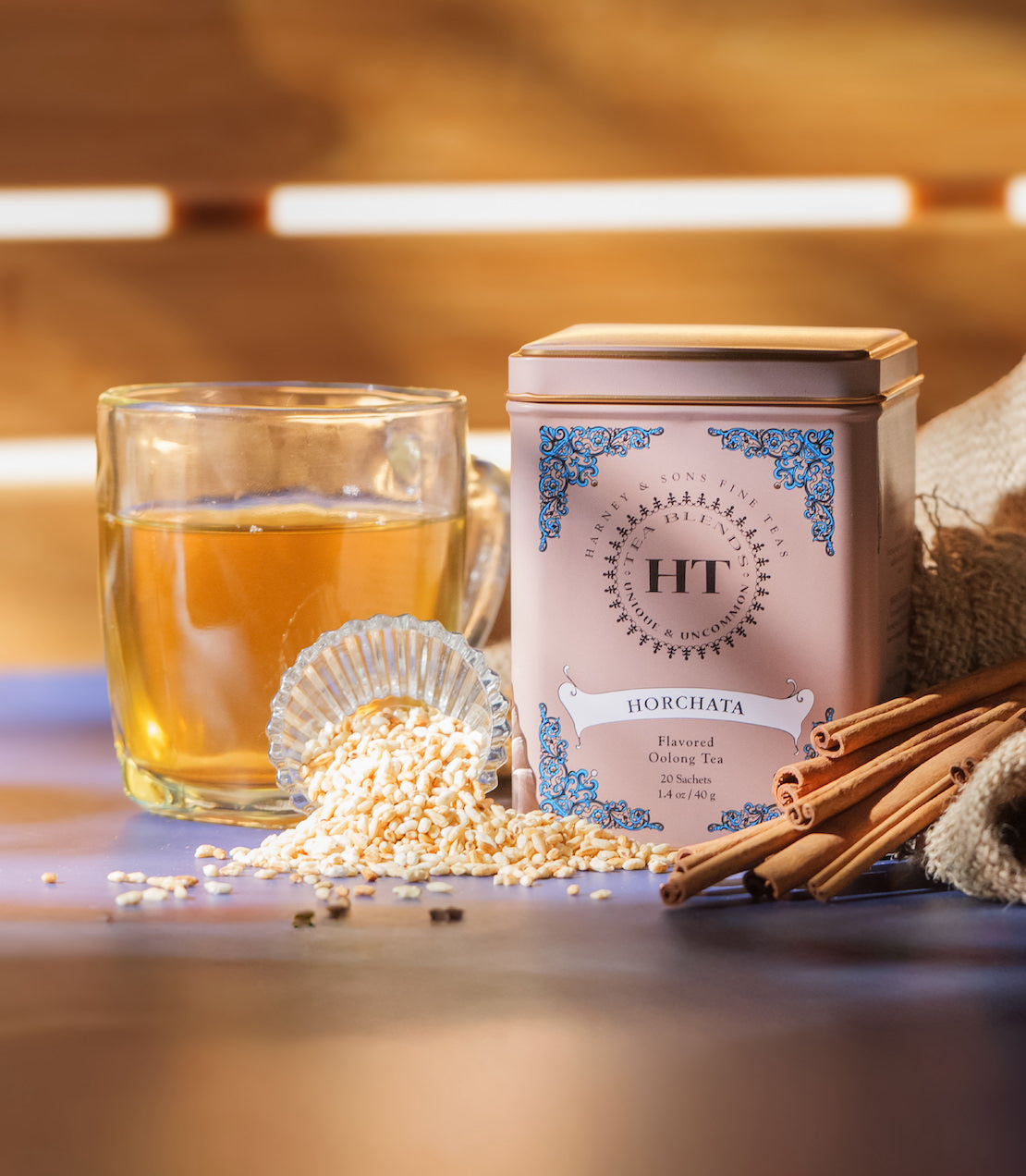 HT Horchata tin with 20 sachets, glass of horchata, cinnamon sticks, and sesame seeds on a wooden surface.