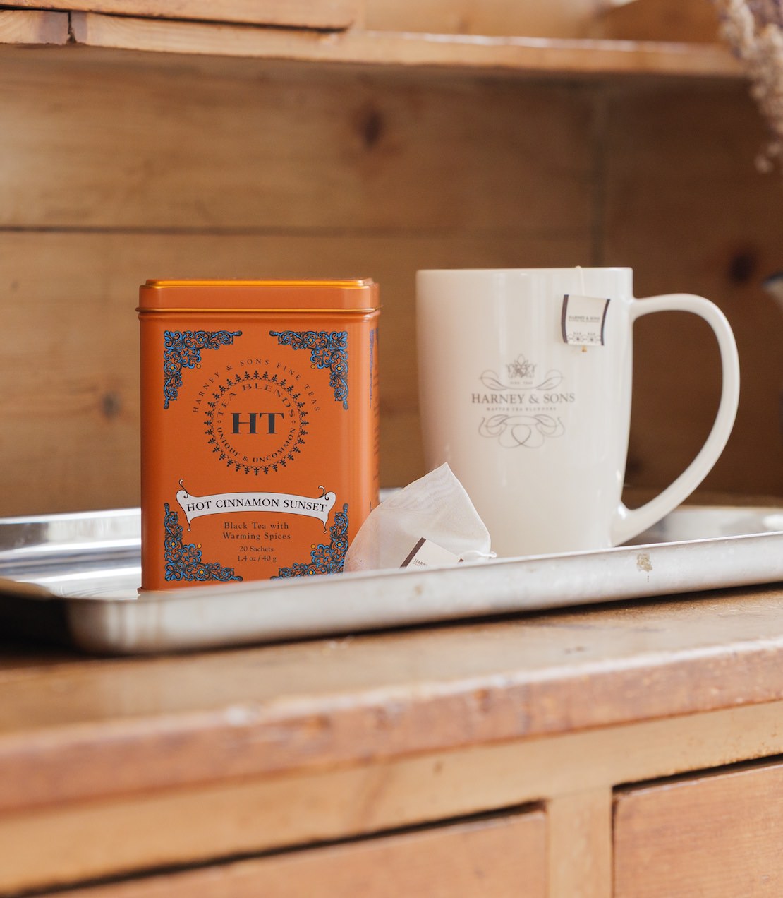 Hot Cinnamon Sunset HT Tin and Harney & Sons mug on a metal tray on top of a wooden counter.
