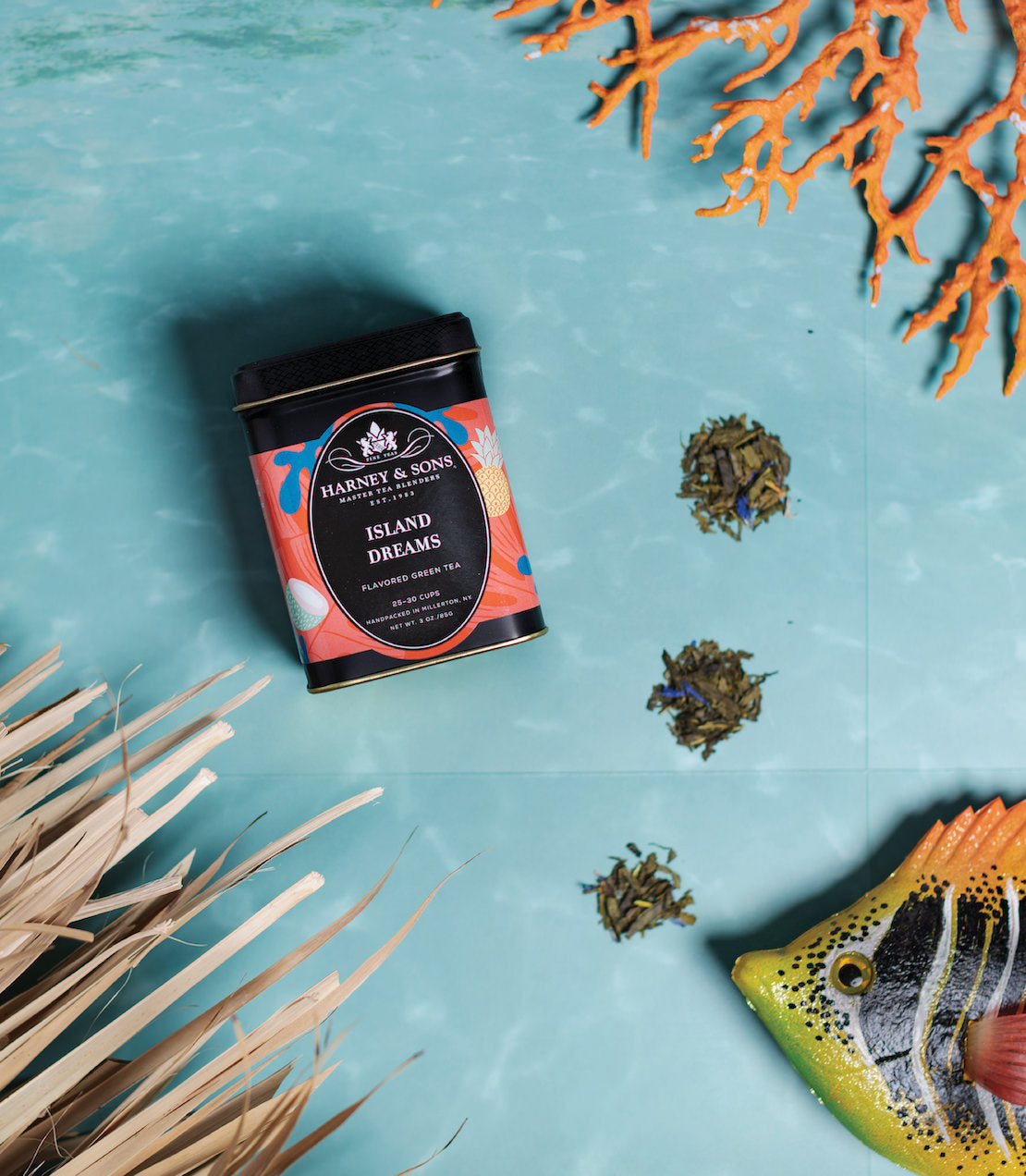 "Harney & Sons Island Dreams tea tin on a turquoise surface with coral and tropical fish decor.