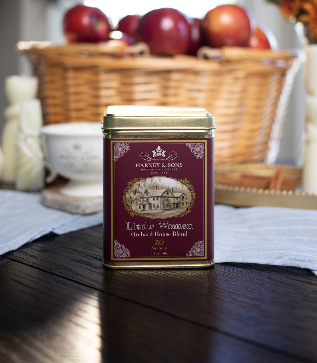 Little Women Orchard House Blend tea tin on a wooden surface with apples in the background.