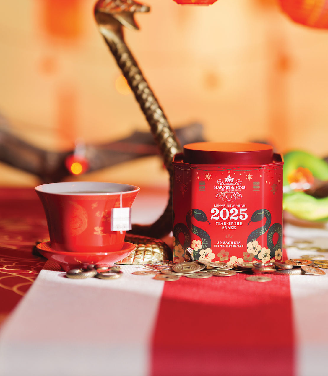 Red tea tin for Lunar New Year 2025, Year of the Snake, with decorative elements and a tea cup on a festive table.
