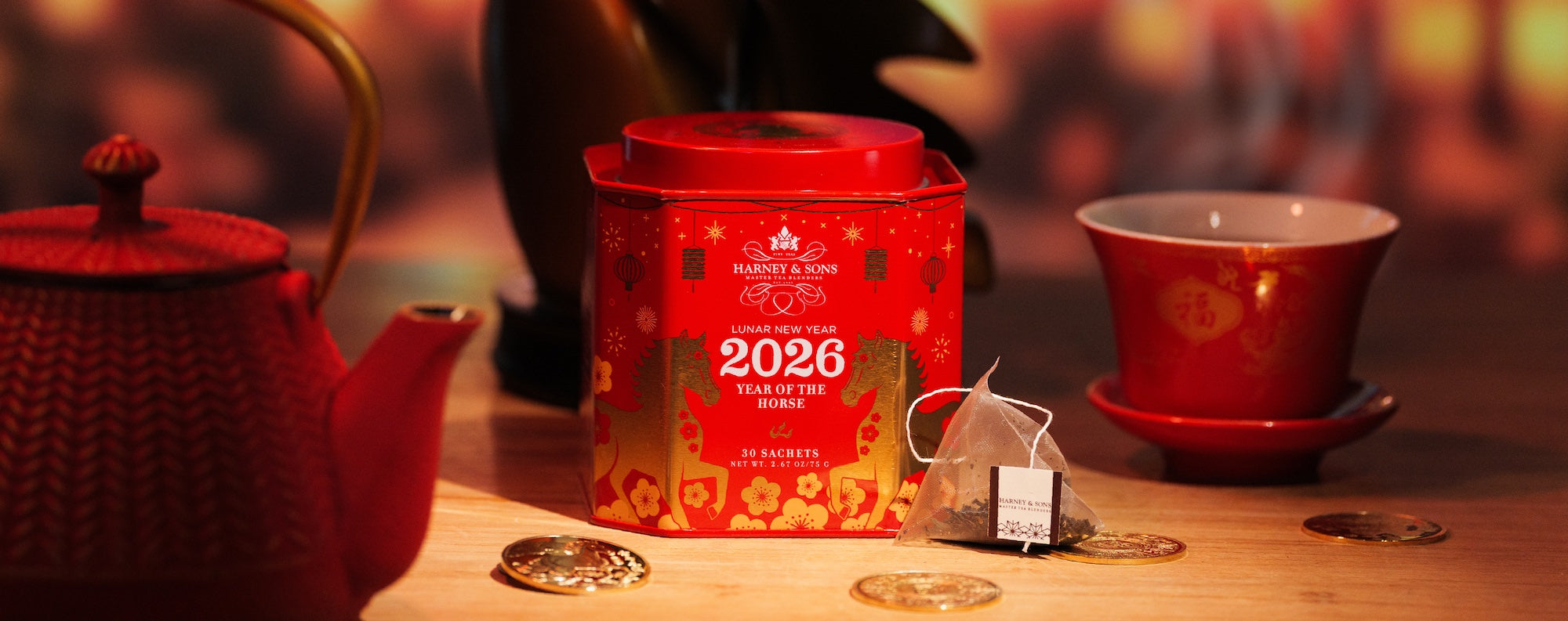 Red tea canister with 'Lunar New Year 2026' design on a wooden table with a teapot and cup.