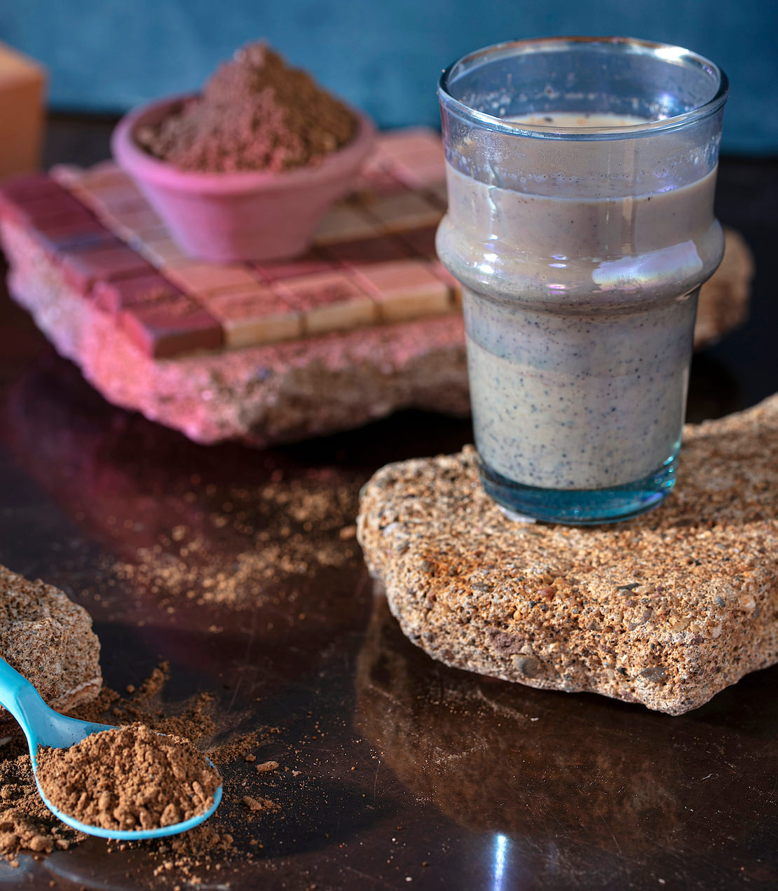 Glass of Organic Chaga Chai on a textured surface, with a bowl of chaga powder and a spoon nearby.