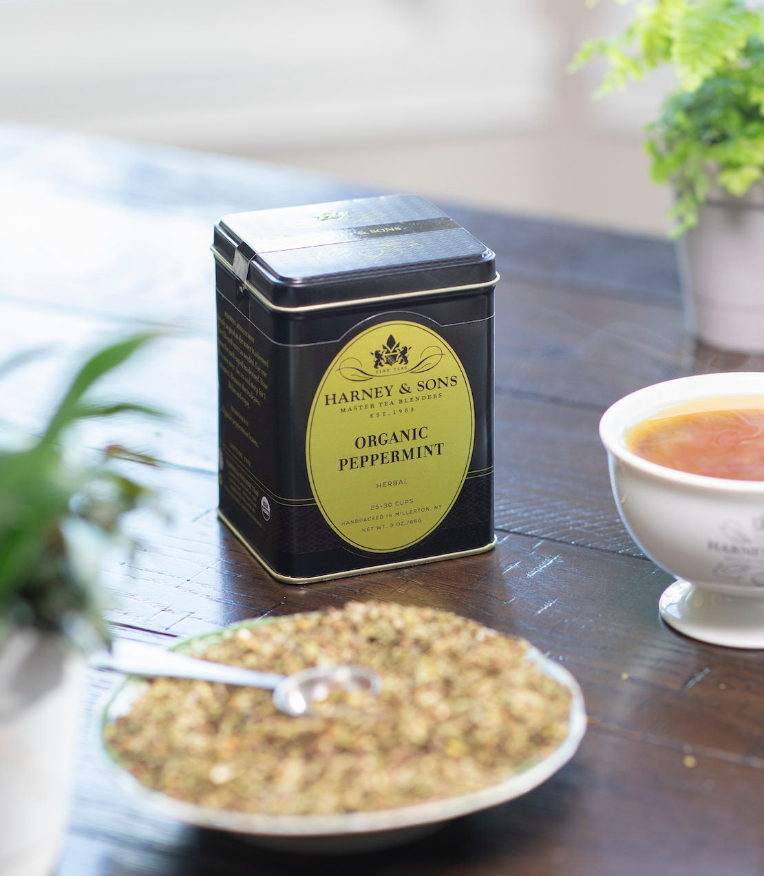 Organic Peppermint tea tin on a table with a bowl of tea leaves and a cup of tea.