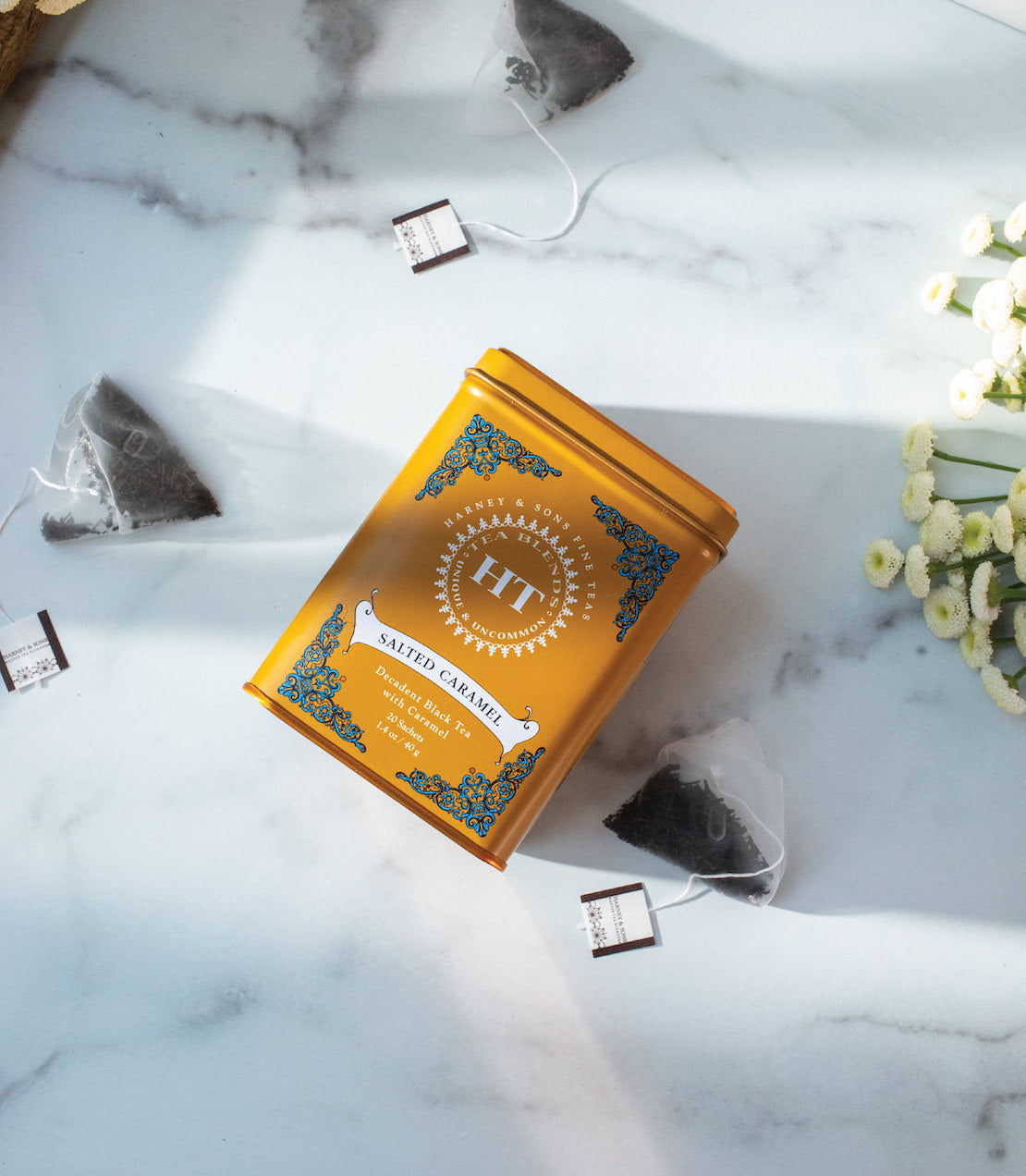 HT Tin of 20 Salted Caramel tea sachets on a marble surface, surrounded by tea bags and flowers.