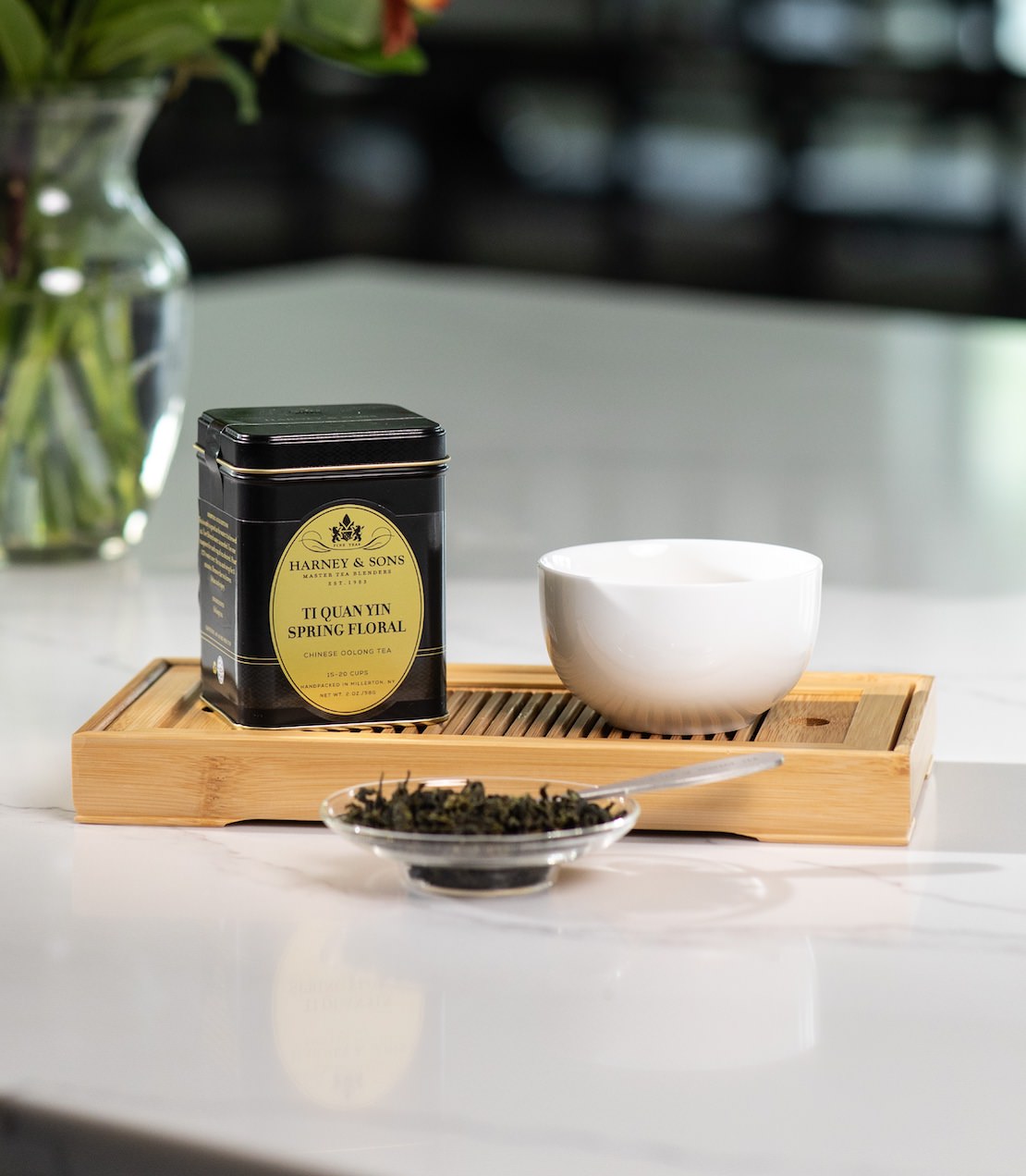 Ti Quan Yin Spring Floral tea tin on a wooden tray with tea cup and tea leaves. 