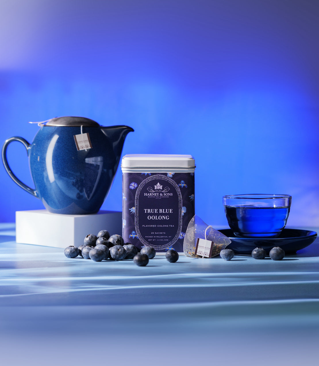 True Blue Oolong tea sachets in a tin, with a teapot, blueberries, and a blue cup on a stylish background.