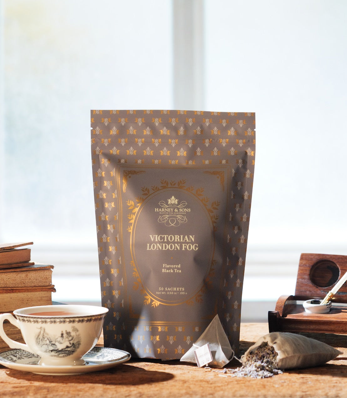 Bag of 50 Sachets labeled 'Victorian London Fog' on a wooden surface with a cup of tea and books in the background.