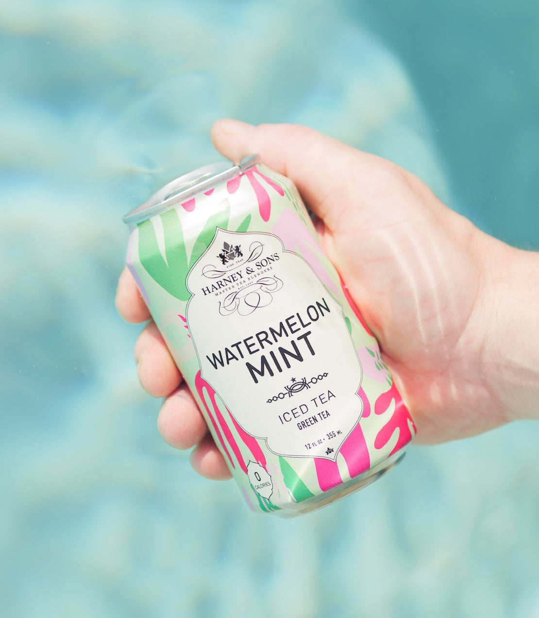 Hand holding a can of 'Watermelon Mint' iced tea with a colorful design against a blurred background.