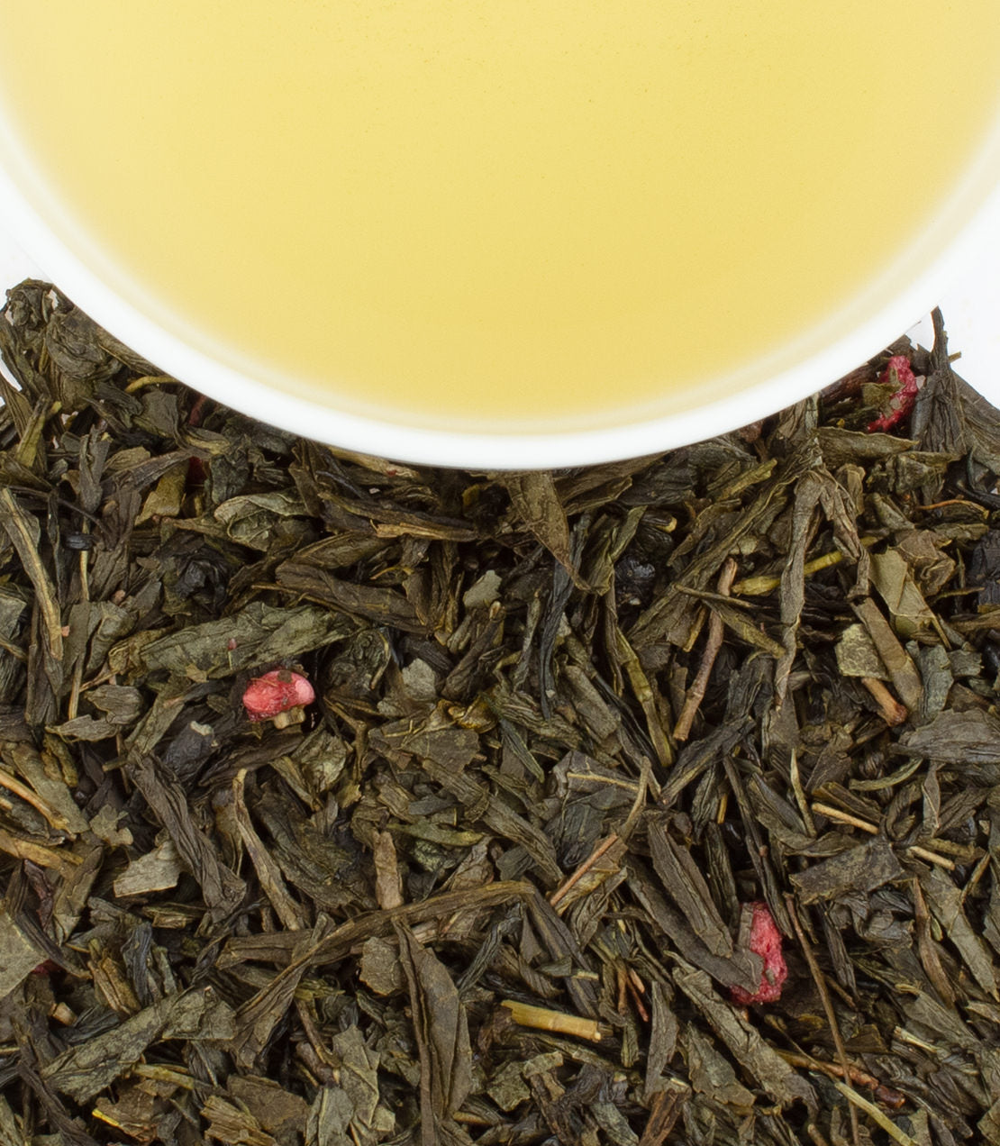 Royal Pomegranate Green Tea sachets with brewed tea in a cup, surrounded by loose tea leaves and pomegranate pieces.