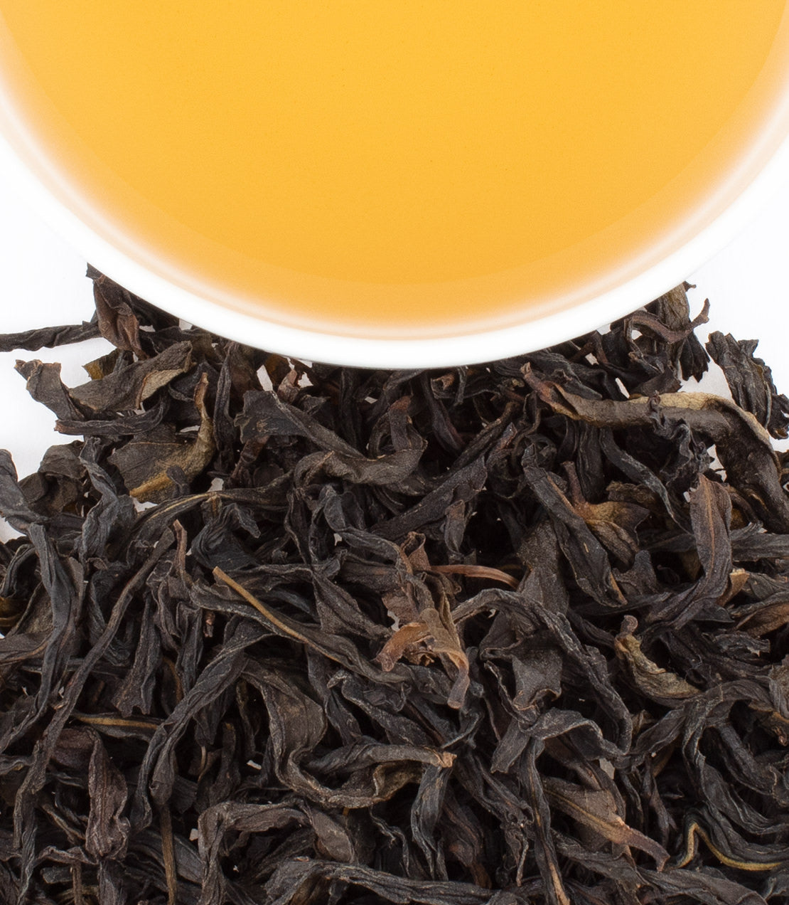 A cup of golden Ya Shi Xiang Oolong tea above a pile of dark, twisted tea leaves.