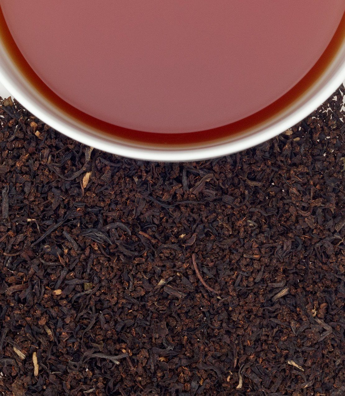 AOH Hibernian Blend tea in a cup, surrounded by loose black tea leaves on a white background.