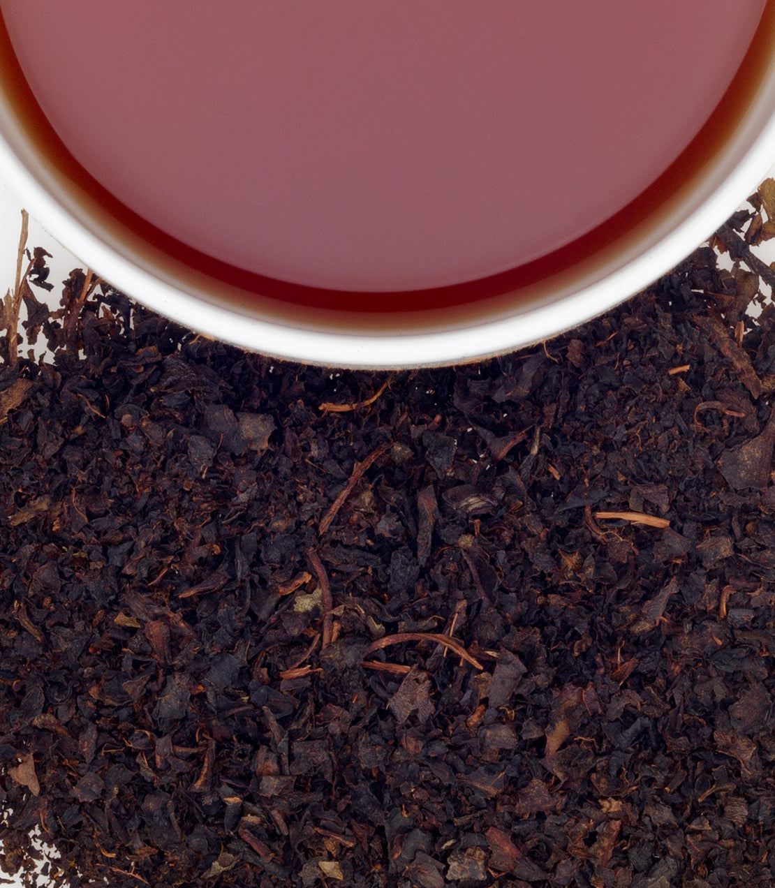 A cup of Amba Thieves Tea beside loose tea leaves, showcasing its rich color and texture.