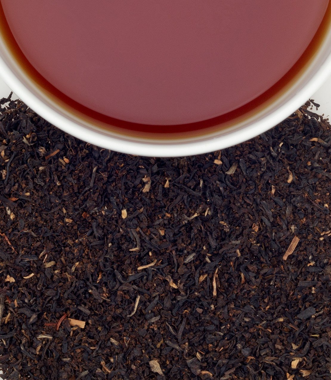 A close-up of brewed Orange Pekoe tea in a white cup, surrounded by loose black tea leaves.