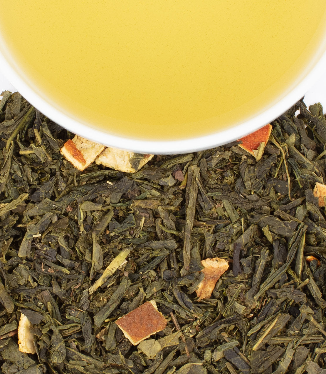 A close-up of loose green tea leaves with citrus pieces, alongside a cup of brewed green tea.