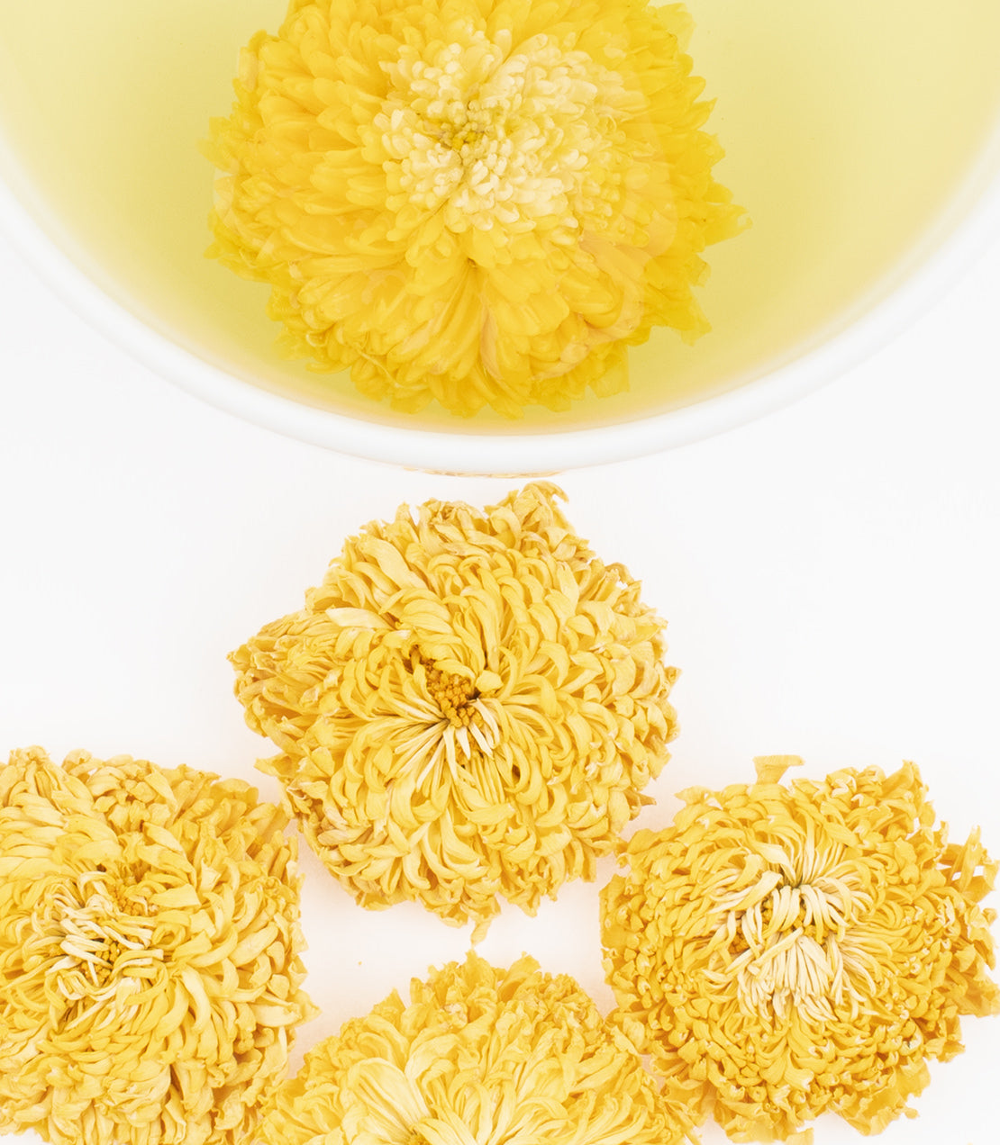 Dried Royal Chrysanthemum flowers arranged around a bowl of yellow chrysanthemum tea.