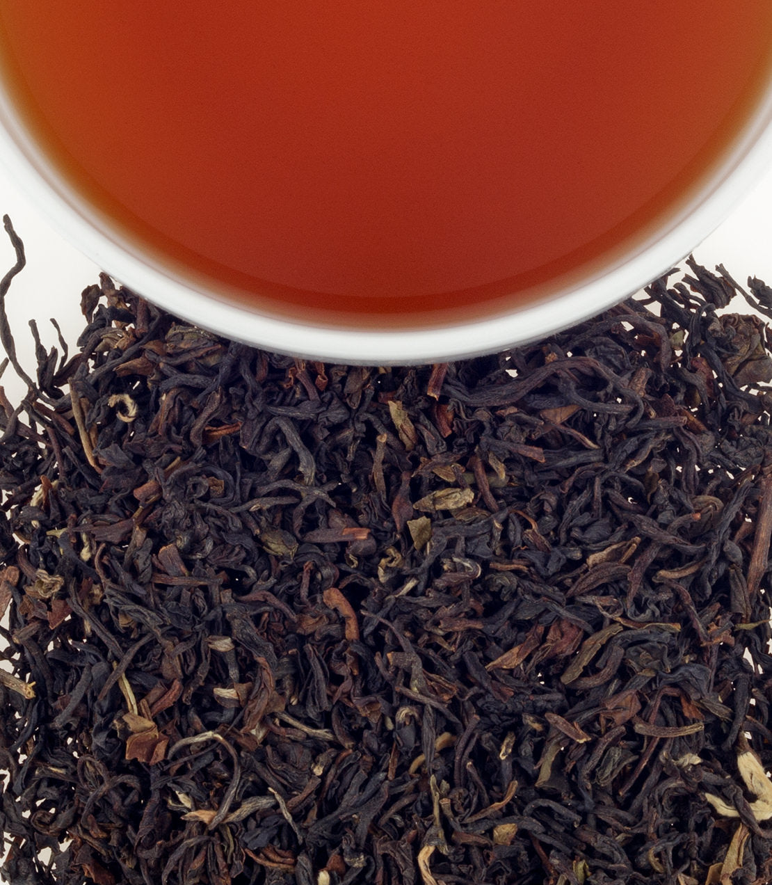 A close-up of dried Indian Nimbu tea leaves with a cup of brewed tea above, showcasing rich color and texture.