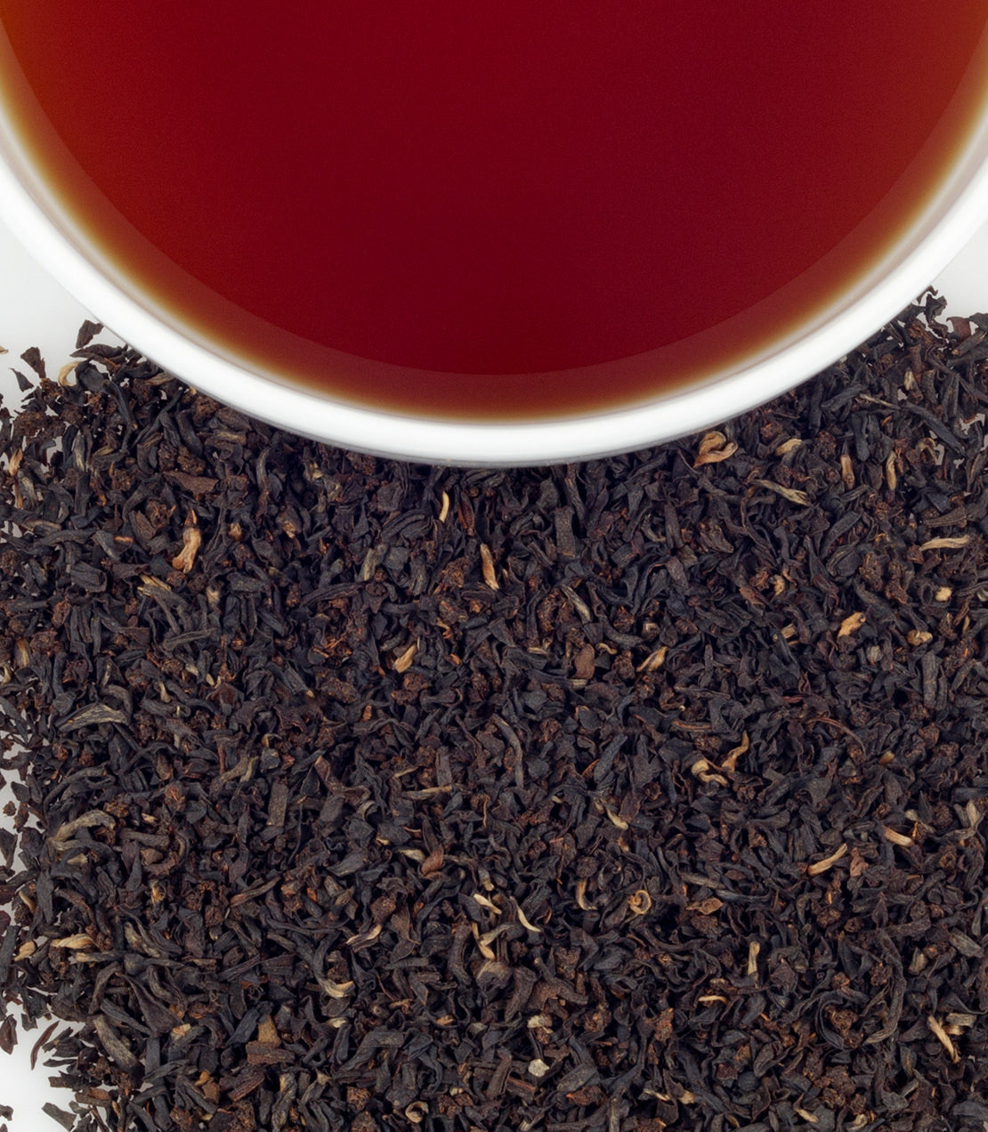 Irish Breakfast tea in a cup, surrounded by loose black tea leaves, showcasing rich color and flavor.