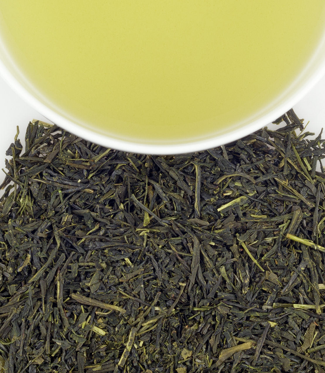 Fresh Japanese Sencha tea leaves with brewed green tea in a white cup above. Rich color and aroma.