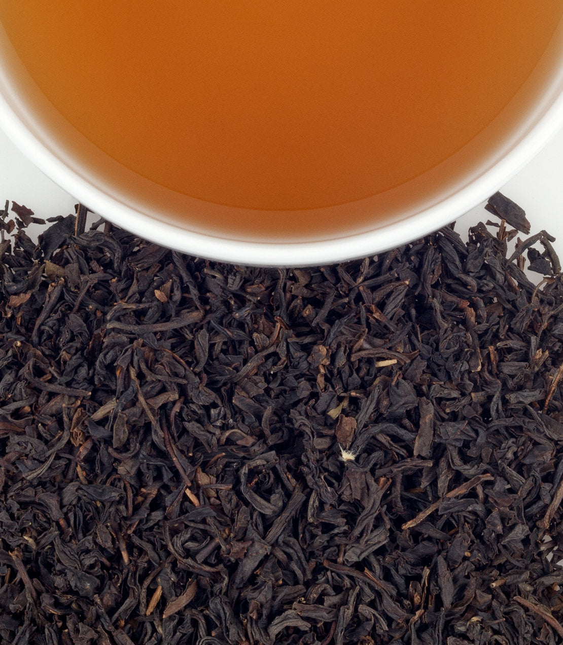 A close-up of dried black tea leaves with a cup of brewed tea above, showcasing rich colors and textures.