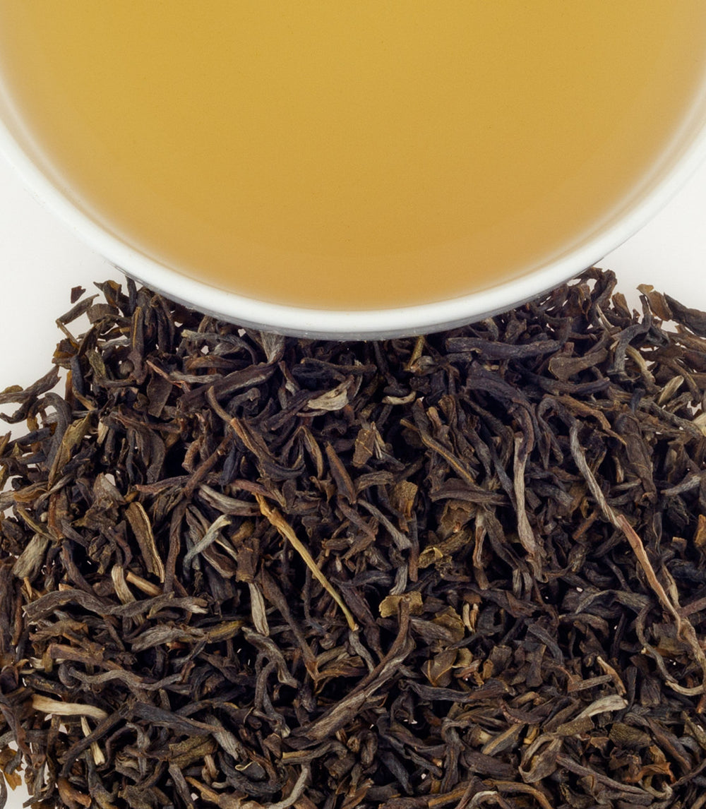 Organic jasmine tea leaves with a cup of brewed tea above, showcasing rich colors and textures.