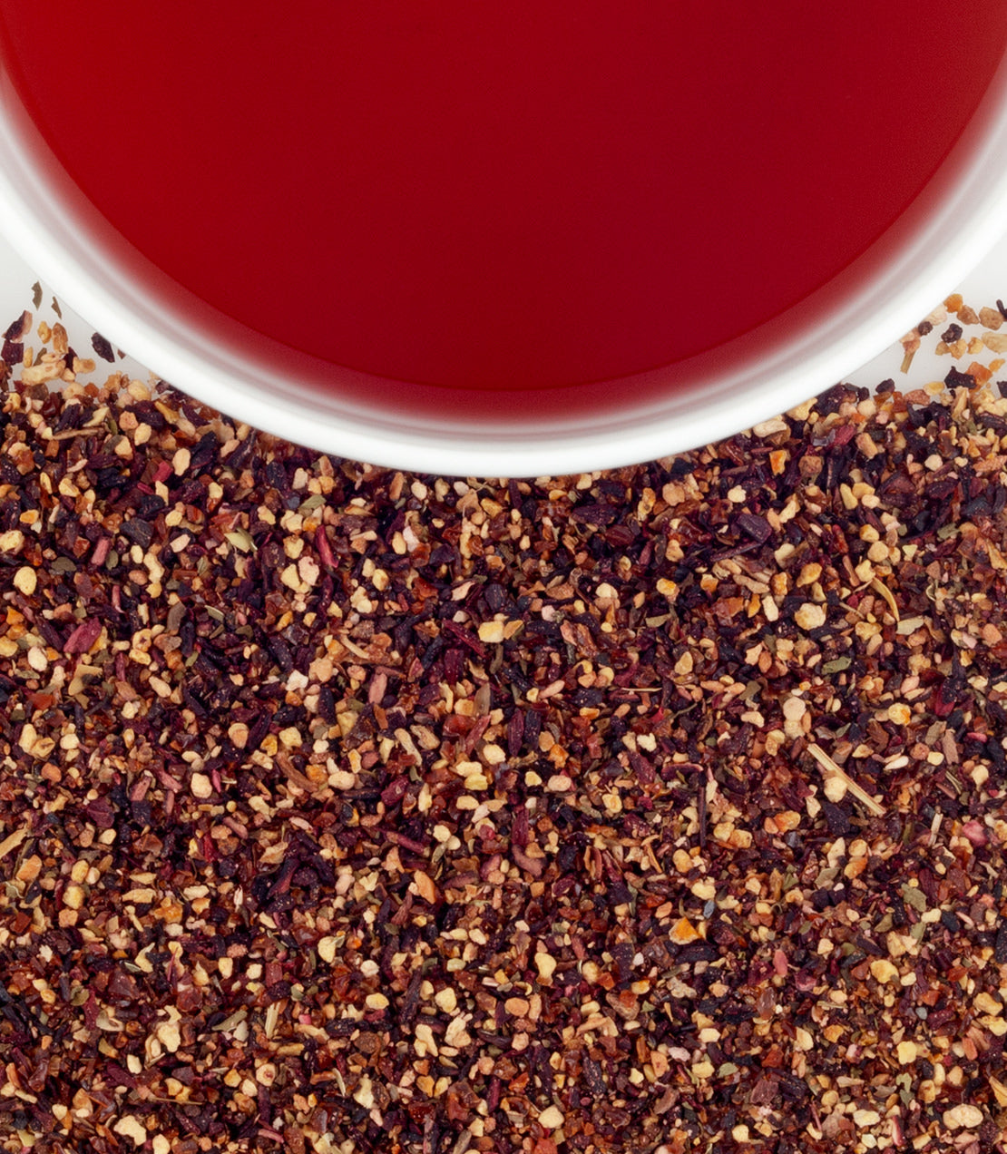 Raspberry herbal tea with vibrant red liquid above a bed of dried raspberry leaves and seeds.