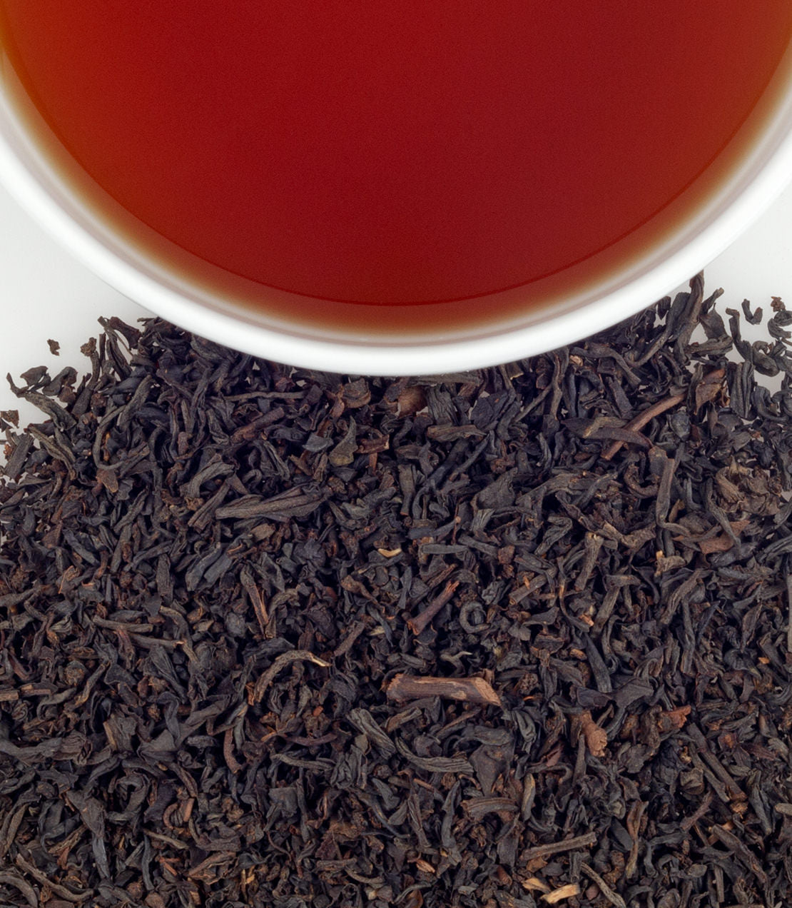 Rich RMS Titanic Blend tea with deep amber liquid above a mound of loose black tea leaves.