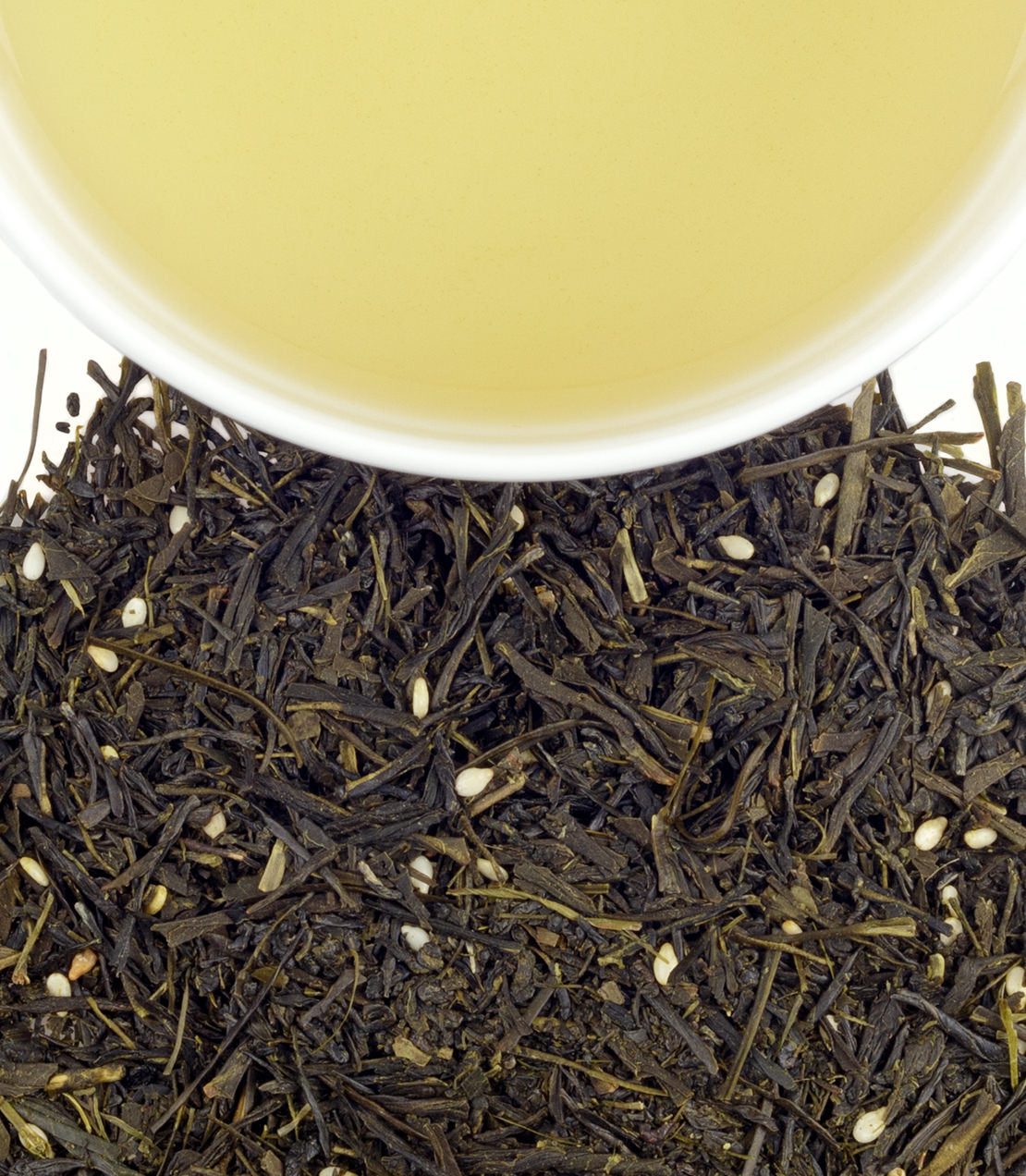 A close-up of loose green tea leaves with a cup of brewed green tea above, showcasing its light yellow color.