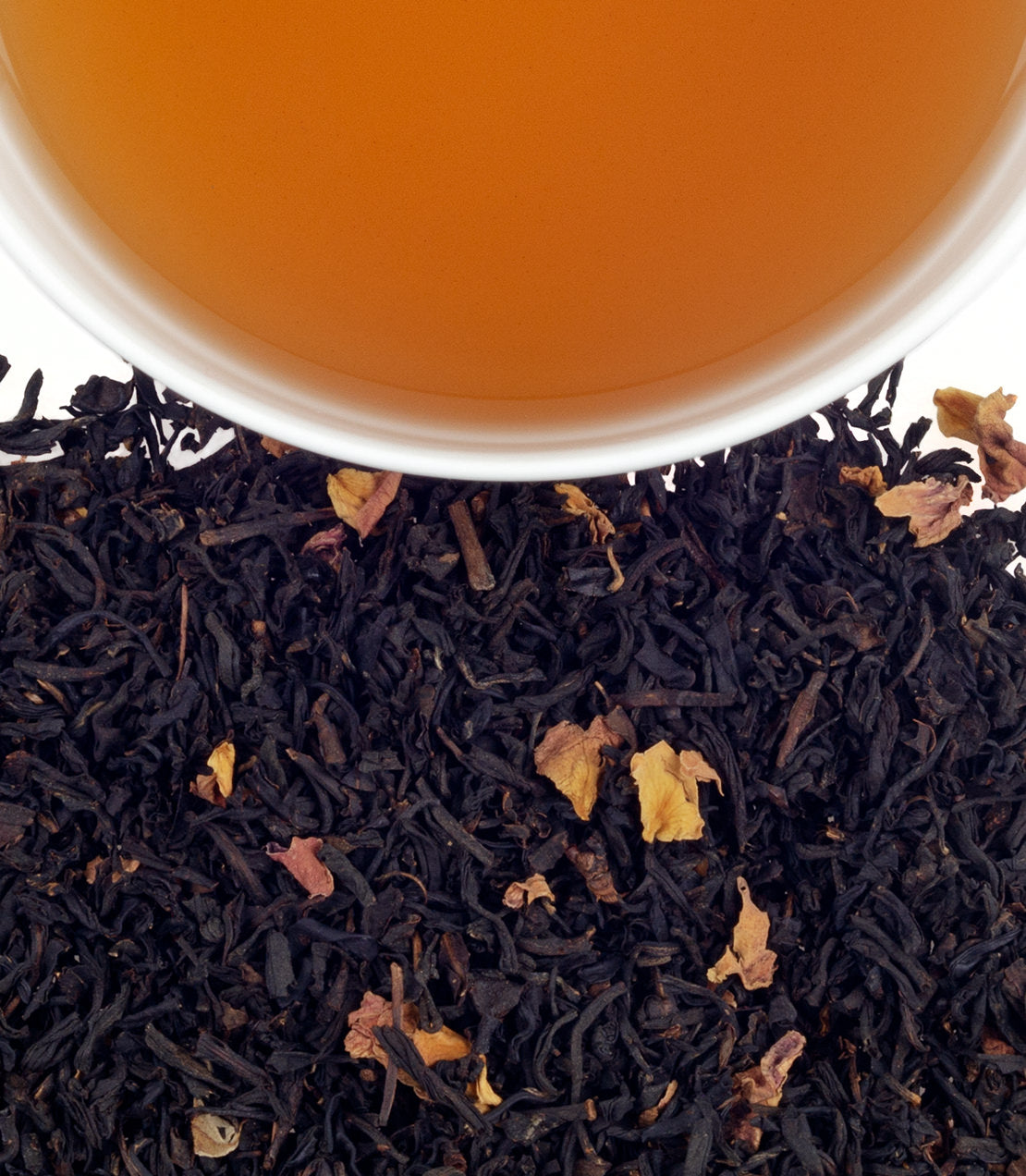 A cup of brewed tea above loose black tea leaves with rose petals, perfect for a romantic Valentine's Day.