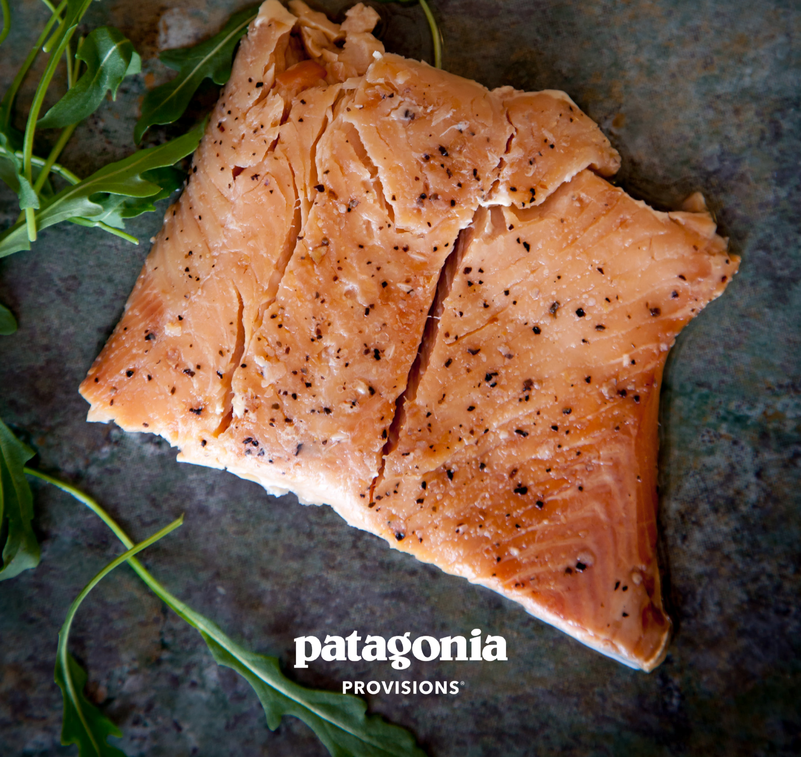 Slice of Patagonia Provisions Wild Sockeye Salmon with seasoning, surrounded by fresh arugula leaves.