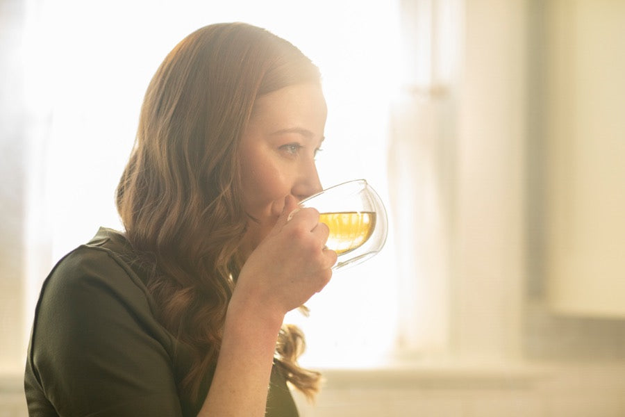 Someone drinking tea from a clear glass cup in morning light