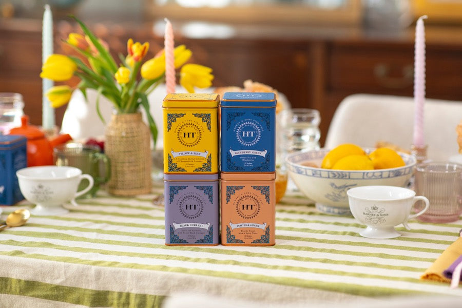 A breakfast table set with Harney & Sons tins, teacups, and yellow tulips