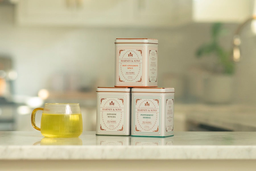 Three Harney & Sons tins stacked on a kitchen counter beside a cup of green tea